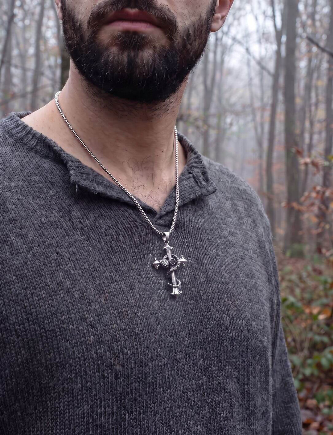 Mann im grauen Strickpullover trägt den Schlangenkreuz-Anhänger an einer Edelstahlkette im nebligen Herbstwald