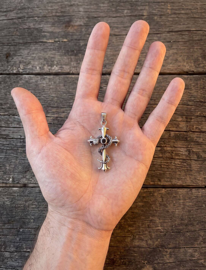 Größenvergleich: Fleur-de-Lis-Kreuz mit Schlange, etwa 5,8 cm hoch, liegt in einer offenen Hand auf Holz