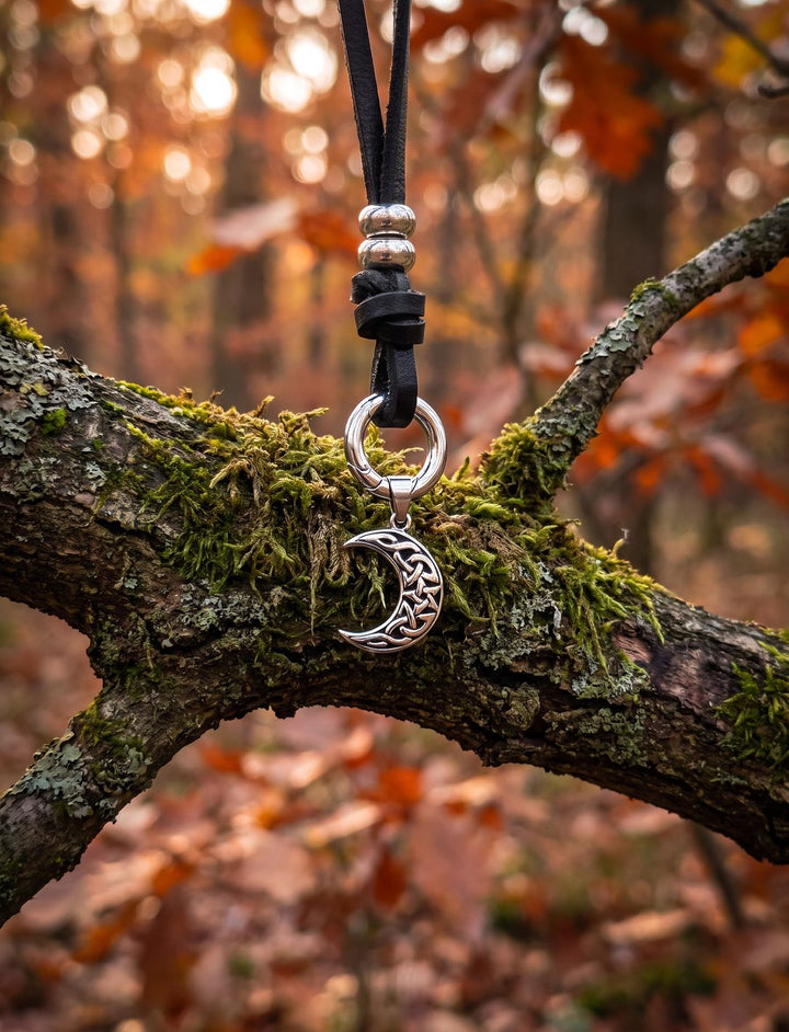 Keltischer Halbmond am Band des Waldläufers mit Federring und Silberperlen an einem moosigen Eichenast im Herbstwald