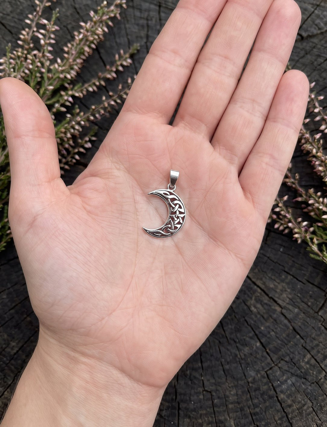 Größenvergleich: Mondsichel-Anhänger mit keltischem Flechtmuster, ca. 3 x 1 cm, in einer offenen Frauenhand über Heide