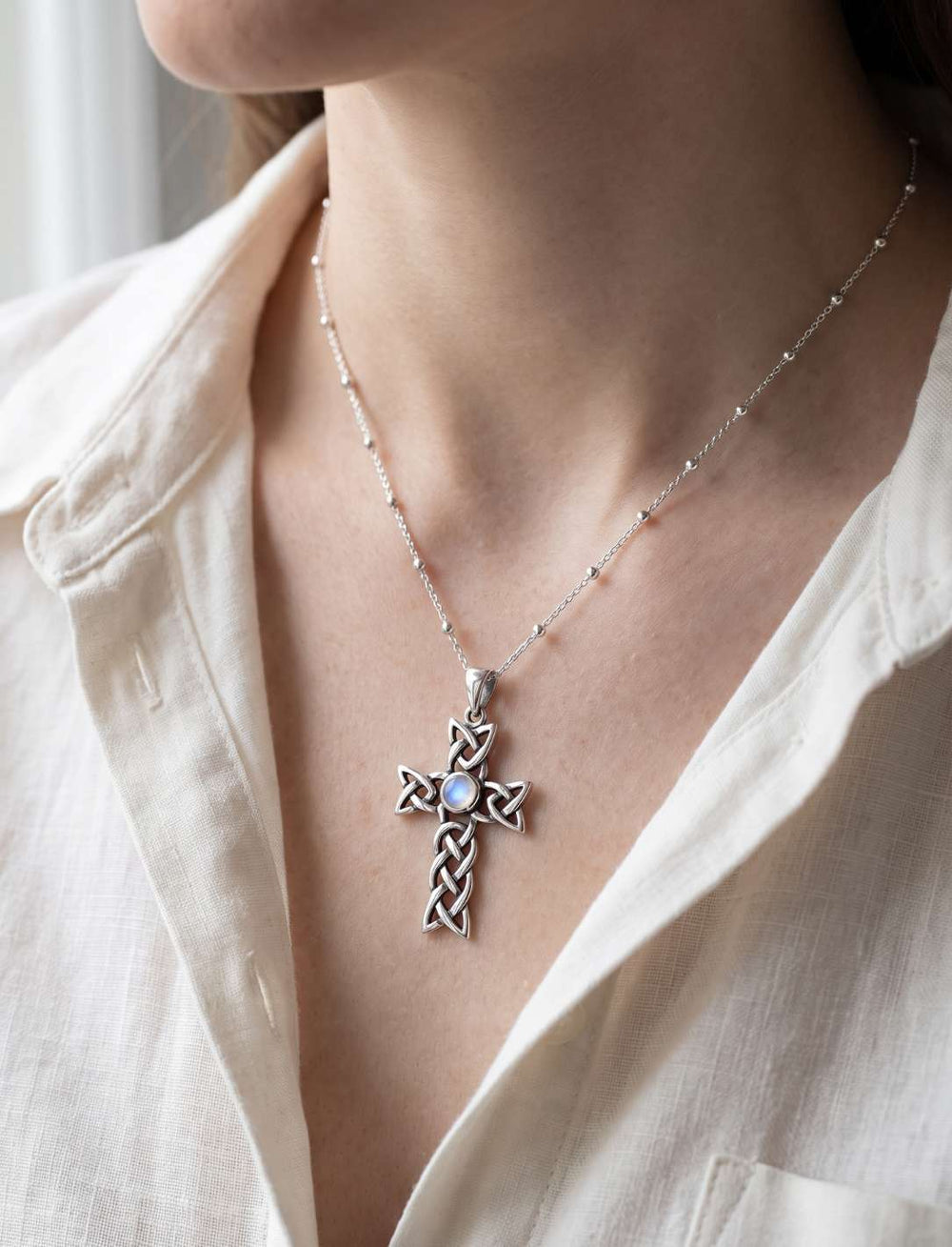 Frau trägt keltisches Silberkreuz mit Mondstein an feiner Perlenkette zu heller Leinenbluse