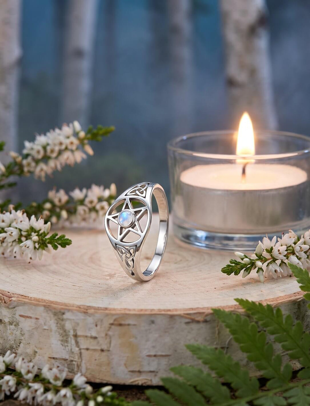 Keltischer Pentagramm Ring mit offenen Triquetras auf einer Birkenholzscheibe zwischen weißer Heide und Teelicht