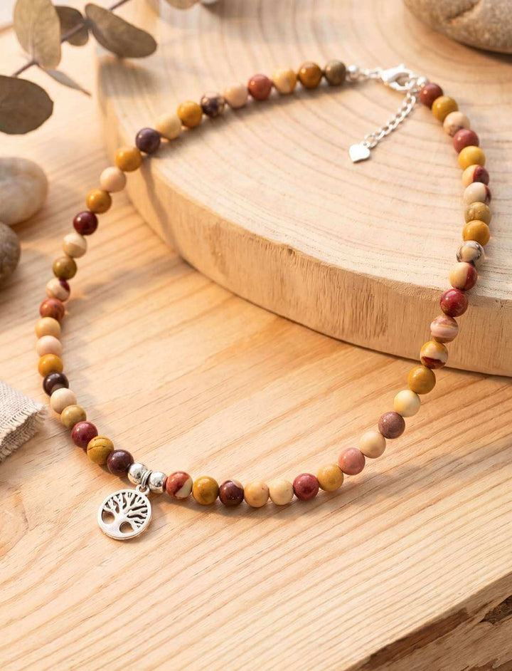 Naturstein Choker mit silbernem Lebensbaum-Anhänger auf hellem Holzbrett neben Eukalyptus