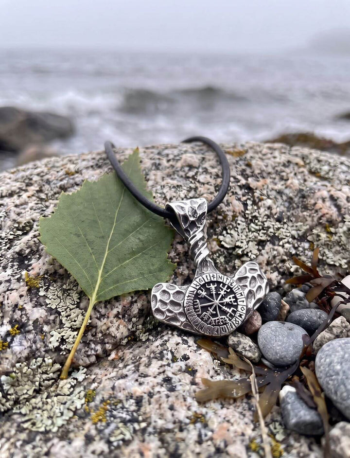 Mjölnir mit Vegvísir und gehämmerten Hammerflügeln an Lederkordel auf Strandfels neben Birkenblatt und Kieseln