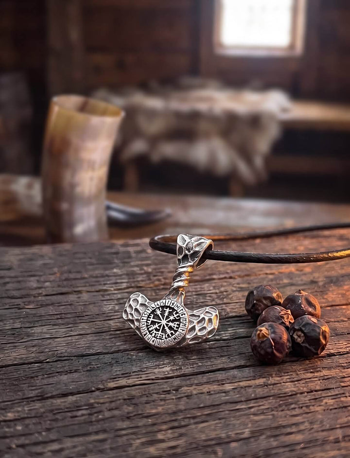 Gehämmerter Hammer des Donnergottes mit Vegvísir an Lederkordel auf altem Holztisch im Langhaus, daneben Wacholderbeeren