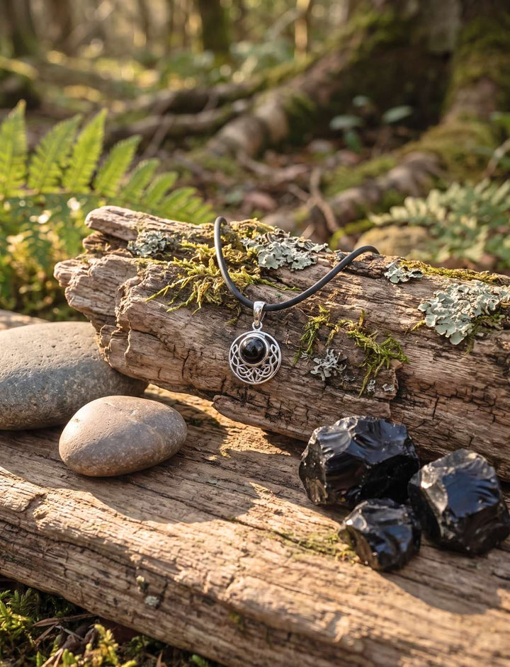 Keltischer Onyx Anhänger an schwarzer Lederkette auf Treibholz, daneben schwarze Rohsteine als Dekoration