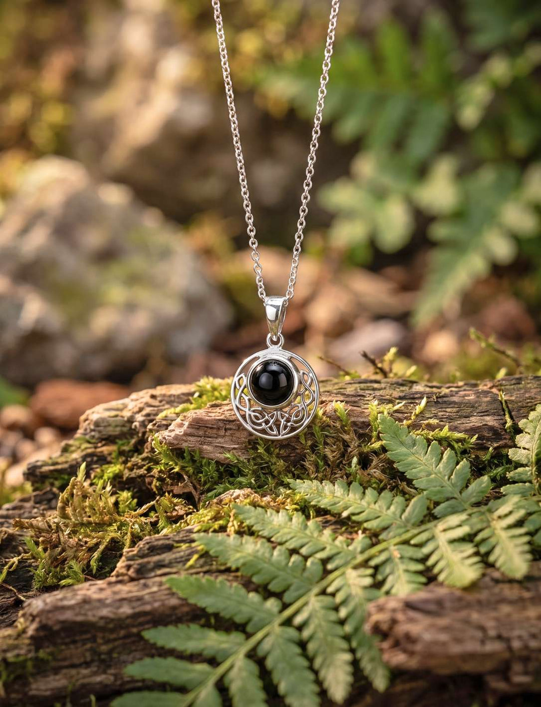 Keltischer Anhänger aus 925 Silber mit Onyx hängt an Silberkette über Farn
