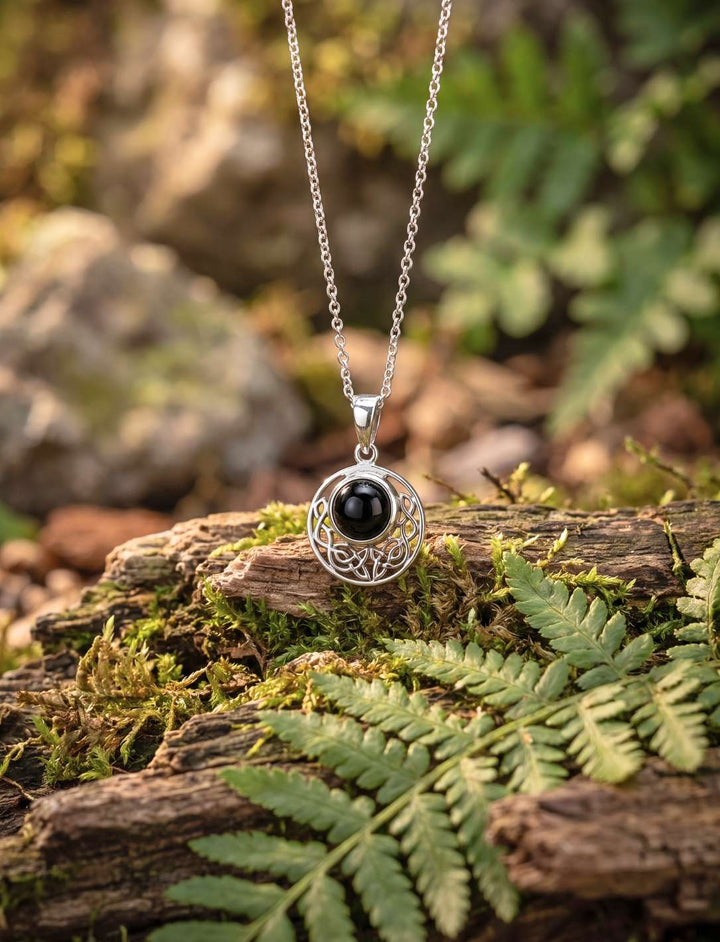 Keltischer Anhänger aus 925 Silber mit Onyx hängt an Silberkette über Farn