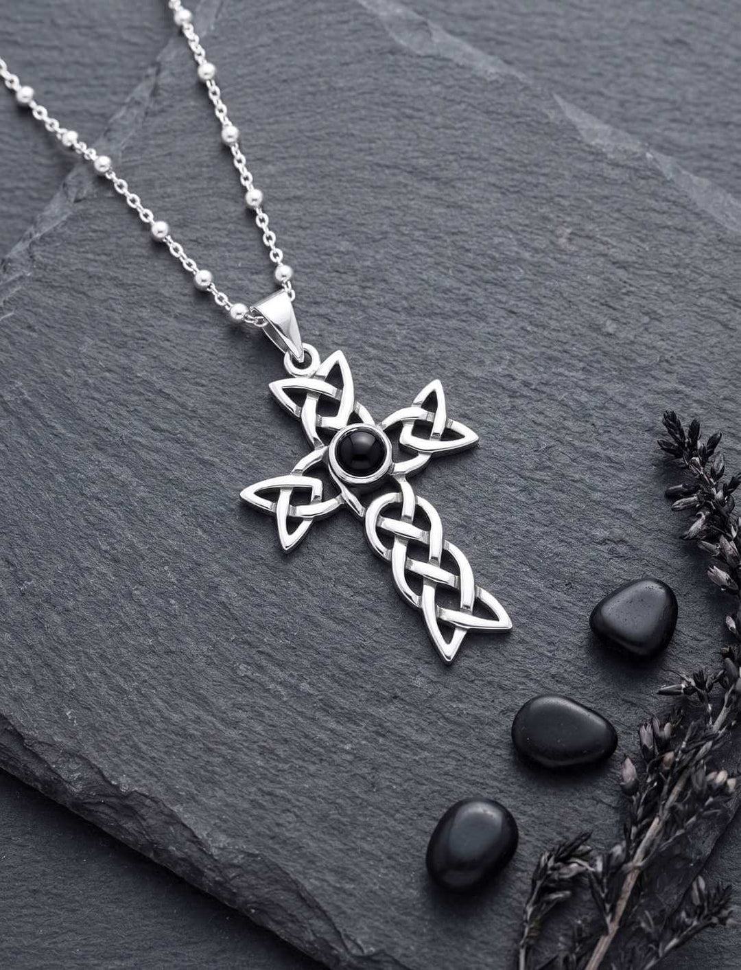 Keltisches Knotenkreuz mit Onyx an feiner Silberkette auf Schiefer neben schwarzen Kieseln