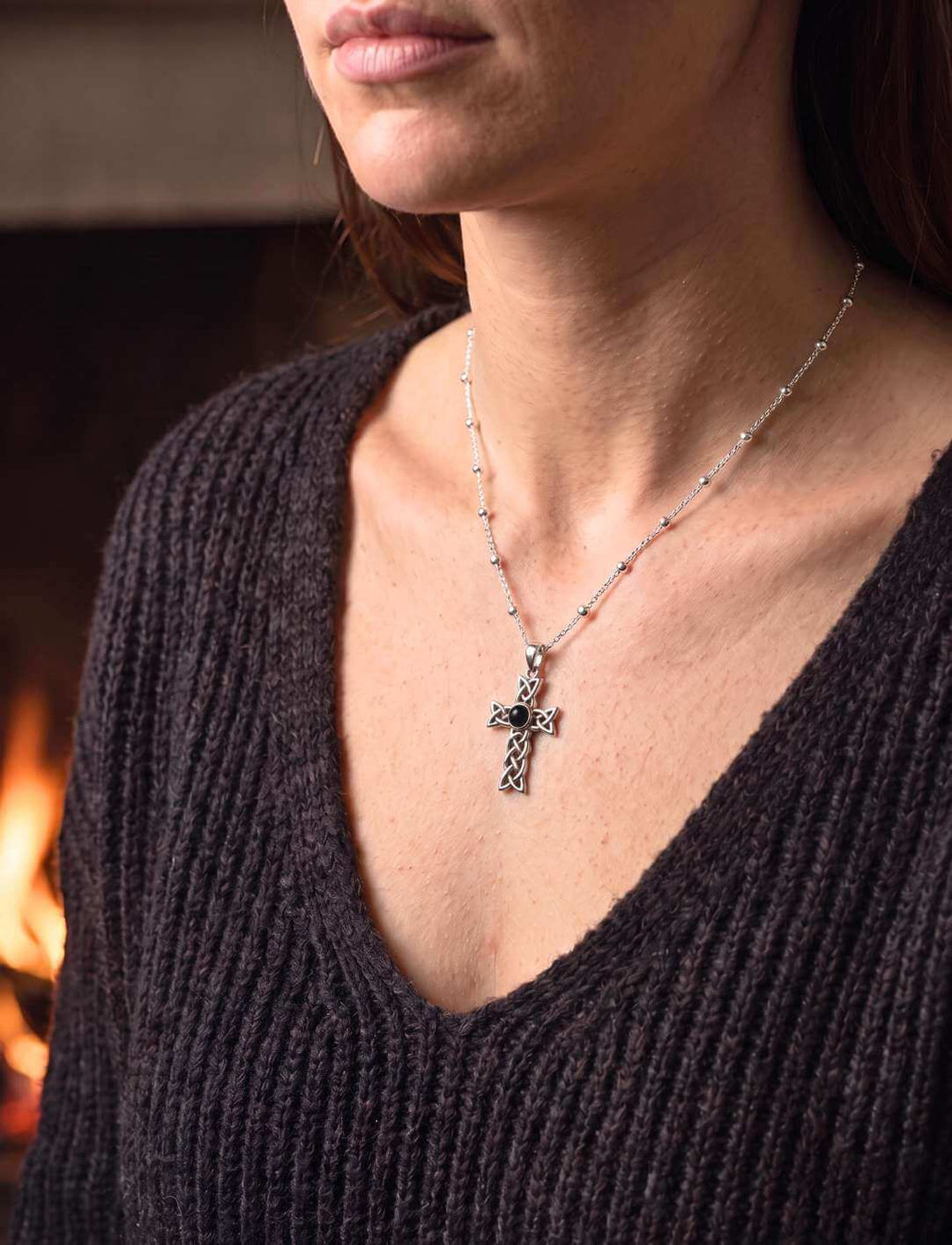Frau am Kaminfeuer trägt keltisches Silberkreuz mit Onyx an feiner Silberkette zum Strickpullover