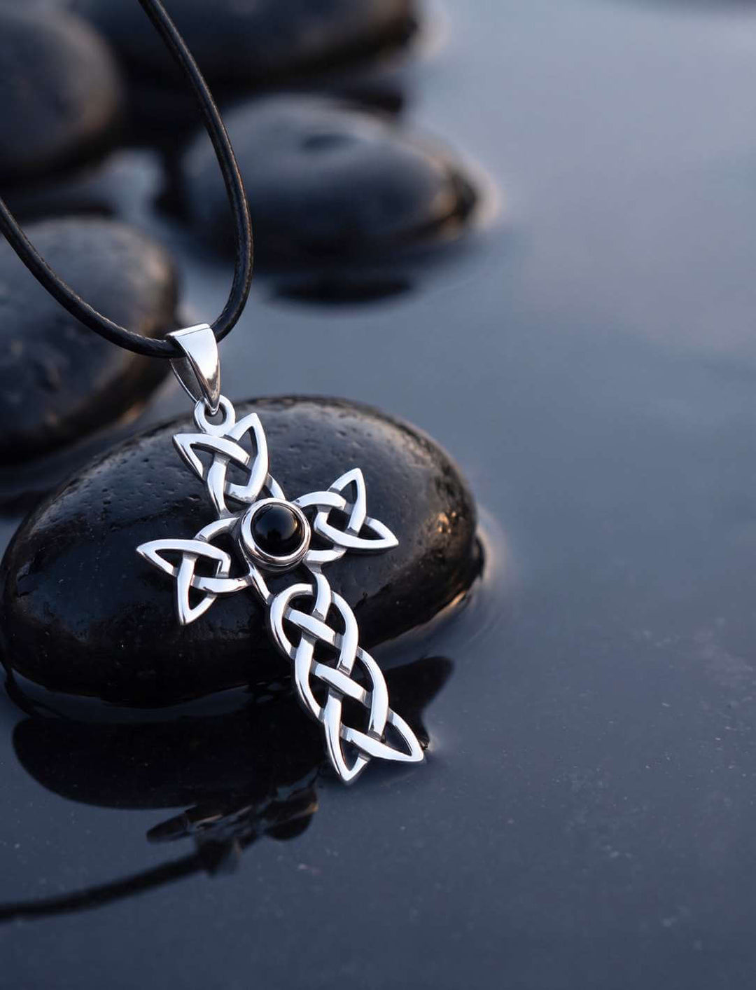 Onyx Anhänger aus Silber mit keltischem Knotenkreuz auf schwarzem Kiesel in der blauen Stunde