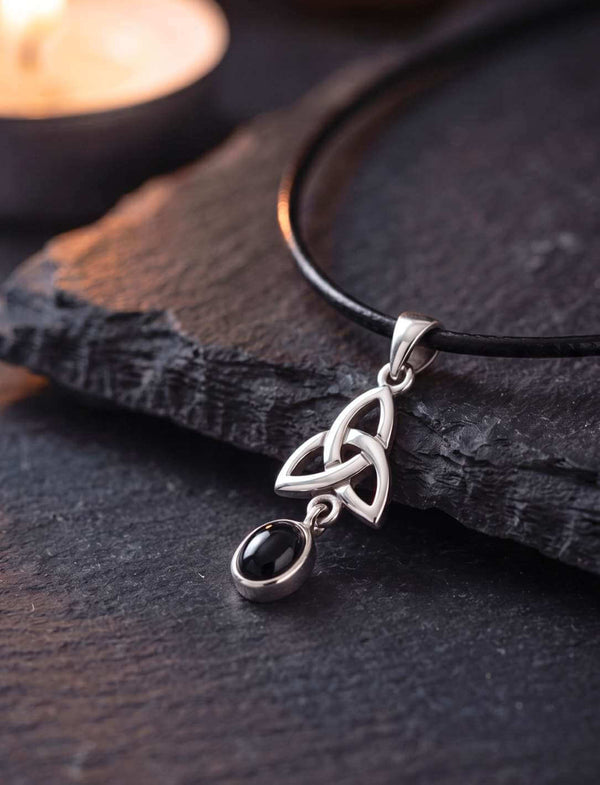 Onyx Anhänger aus Silber mit keltischem Triquetra-Knoten auf dunklem Schiefer im Kerzenlicht