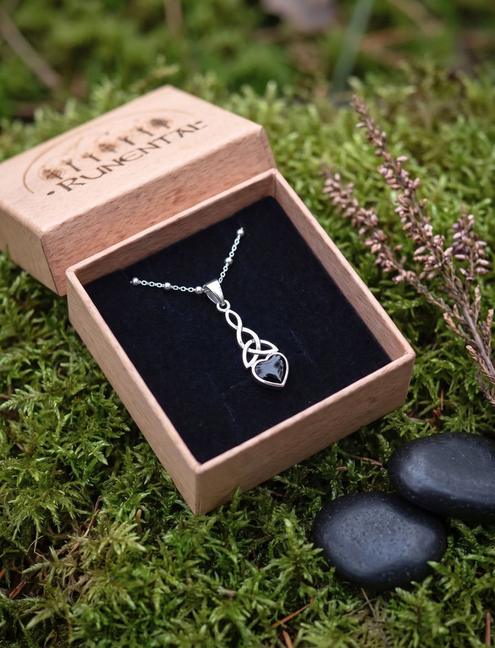 Keltisches Herz aus Silber und Onyx in einer offenen Runental Geschenkbox auf Moos neben schwarzen Kieseln