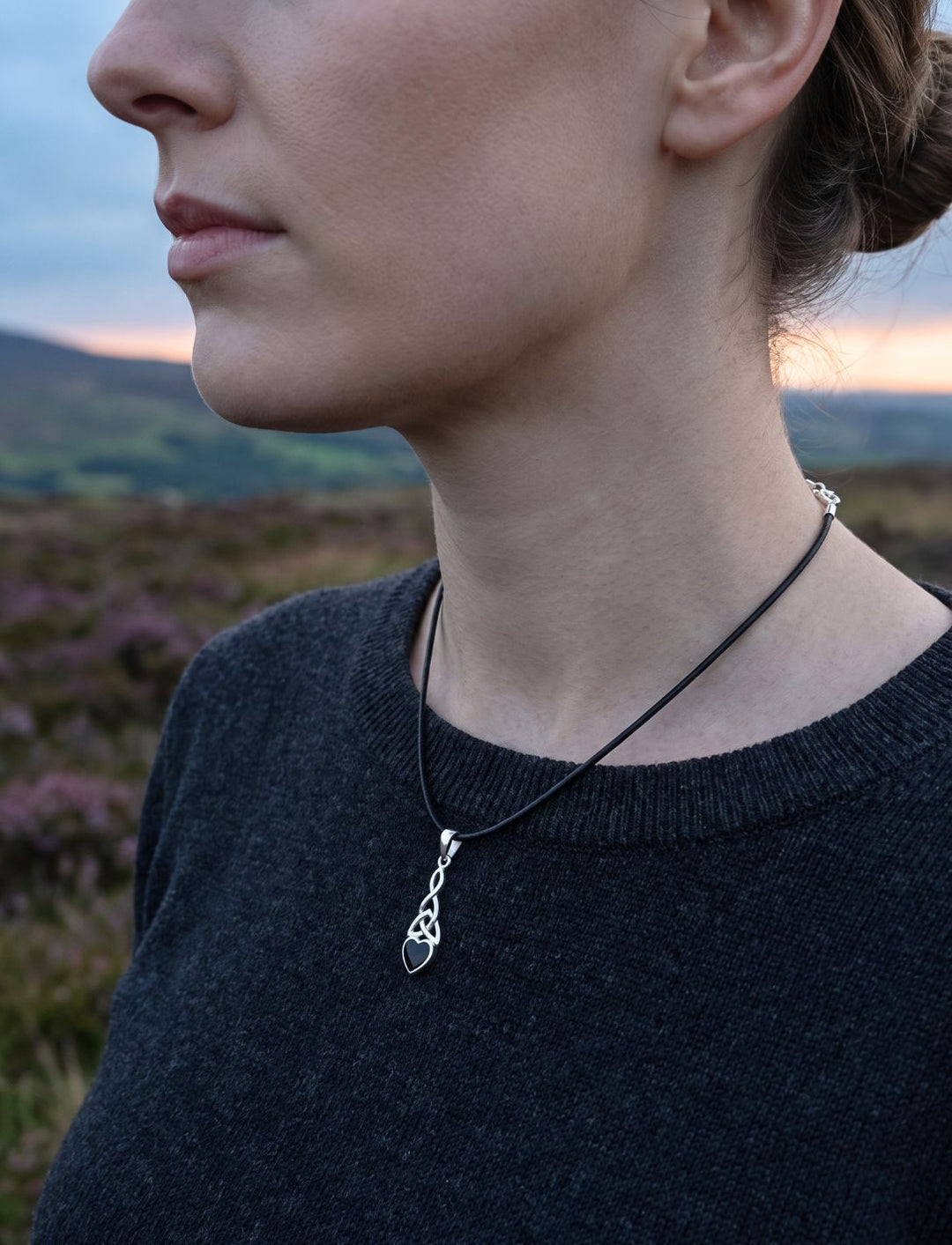 Frau in der Abenddämmerung über irischer Heide trägt den Triquetra Anhänger mit Onyx an einer Lederkette