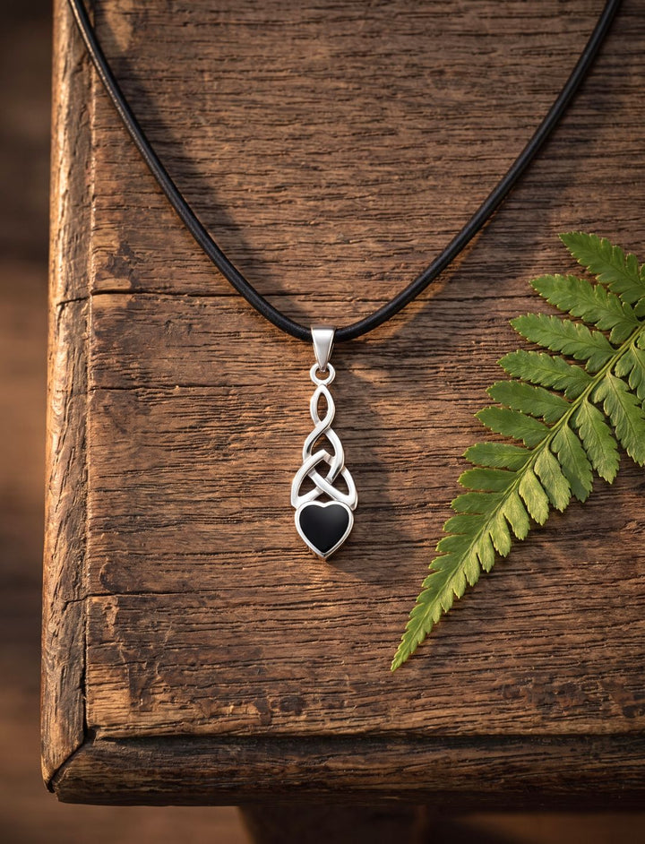 Onyx Herz Anhänger aus Silber mit keltischer Triquetra an schwarzer Lederkette auf altem Eichenholz neben einem Farnblatt