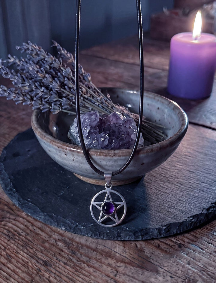 Pentakel mit violettem Amethyst an Lederkette vor einer Steingutschale mit Amethystdruse und Lavendel auf einer Schieferplatte