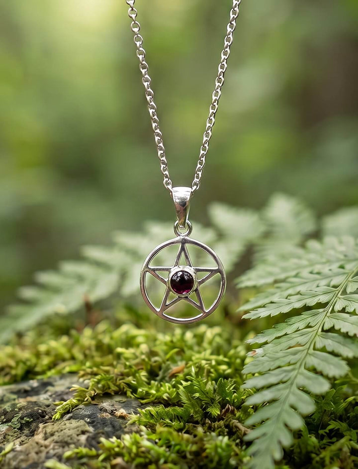 Fünfzackiger Stern im Kreis aus 925 Silber mit Granat-Cabochon an Ankerkette über Moos und Farn im Wald