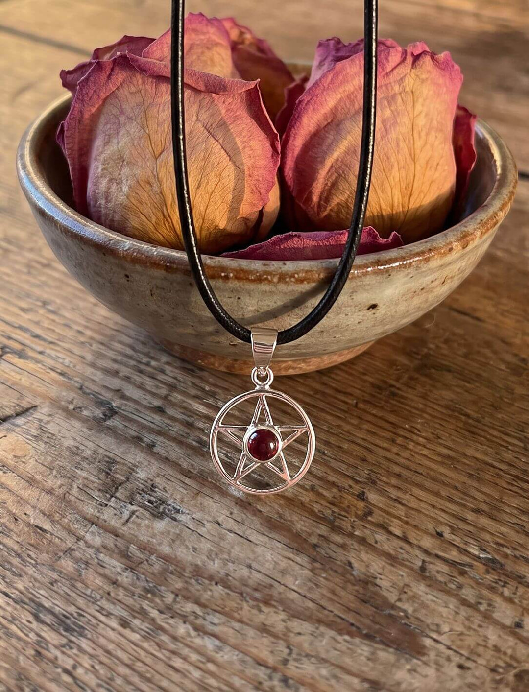 Pentagramm Anhänger mit Granat an schwarzer Lederkette vor einer Keramikschale mit getrockneten Rosenknospen