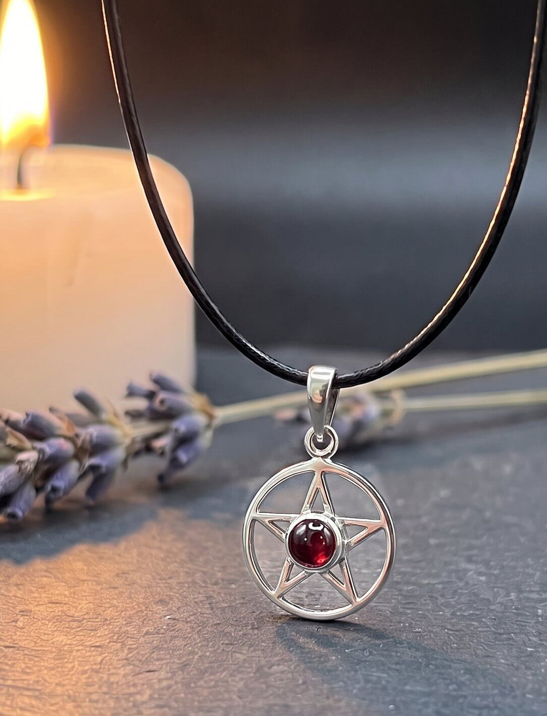 Glutstern: Pentagramm Kette aus Silber mit Granat an schwarzer Lederkordel auf Schiefer neben Lavendel im Kerzenlicht