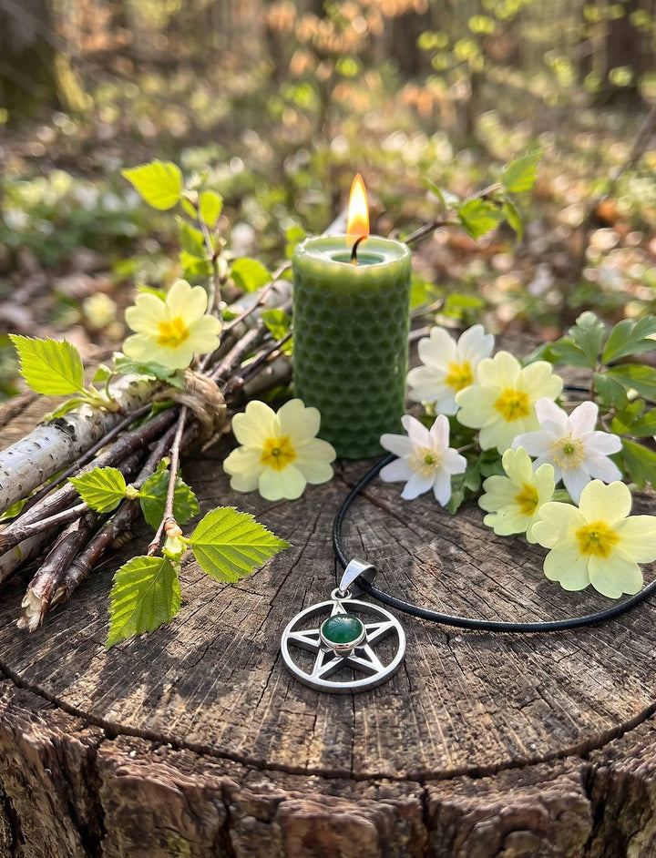 Silberner Fünfstern mit Achat auf einem Ostara-Altar im Wald mit grüner Bienenwachskerze, Primeln und Birkenzweigen