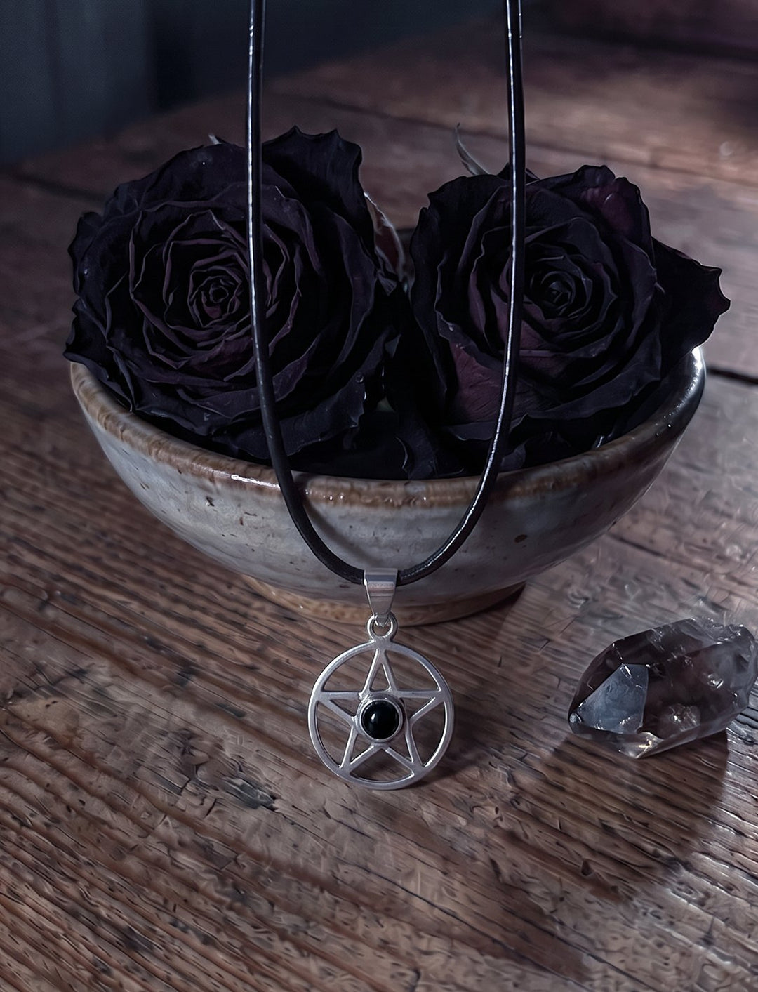 Nachtstern: Pentagramm Kette aus Silber mit Onyx an schwarzer Lederkordel vor dunklen Rosen und Rauchquarz