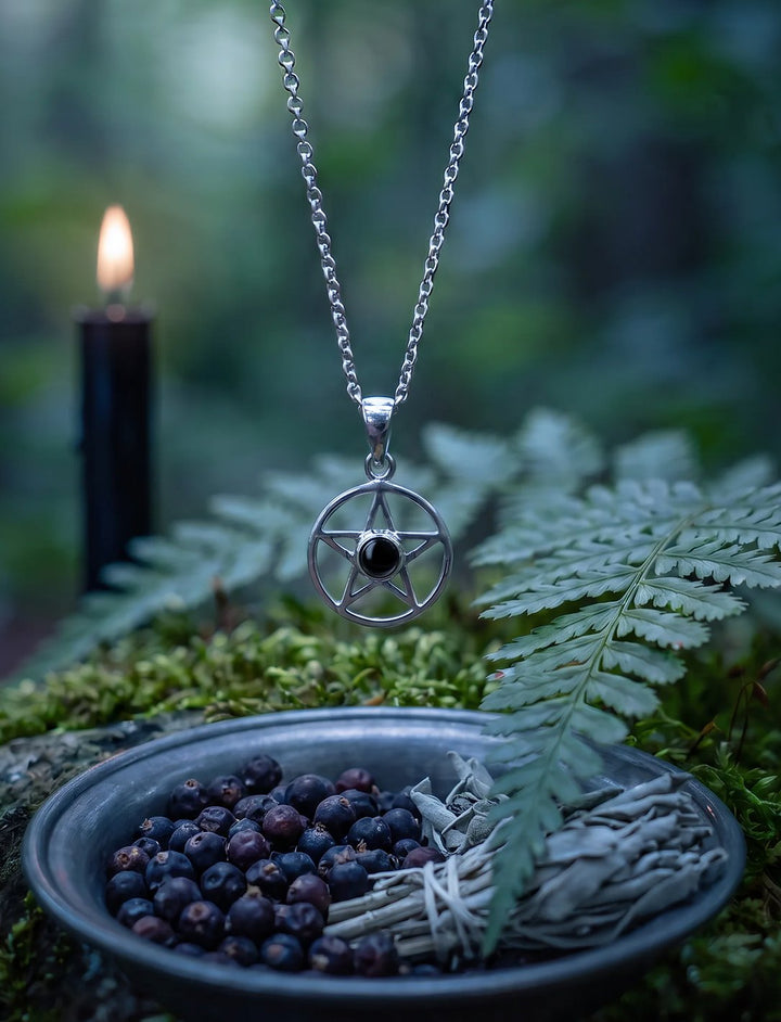 Pentagramm Anhänger mit Onyx an Silberkette über einer Zinnschale mit Wacholderbeeren und Salbei im nächtlichen Wald