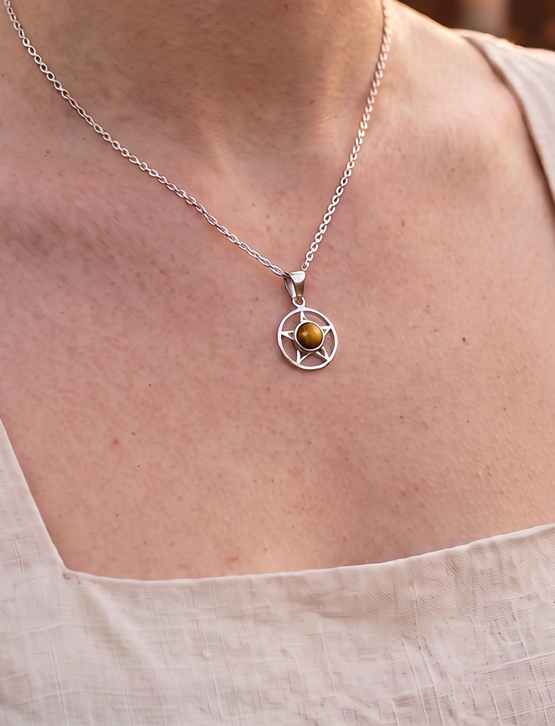 Frau im hellen Leinenkleid trägt das Pentakel mit goldbraunem Tigerauge an feiner Silberkette vor Kerzenlicht