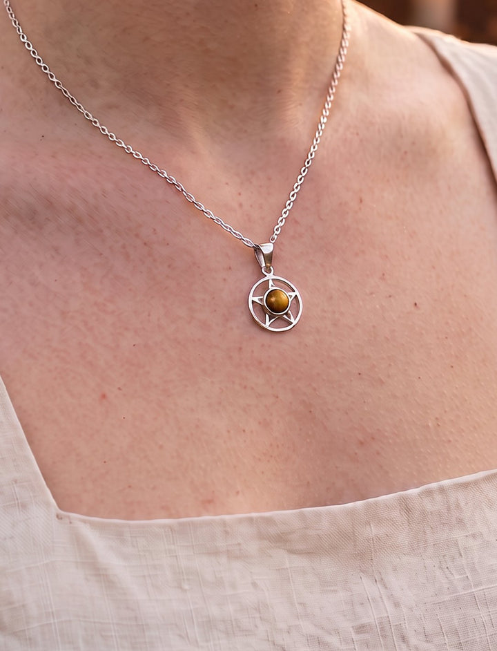 Frau im hellen Leinenkleid trägt das Pentakel mit goldbraunem Tigerauge an feiner Silberkette vor Kerzenlicht