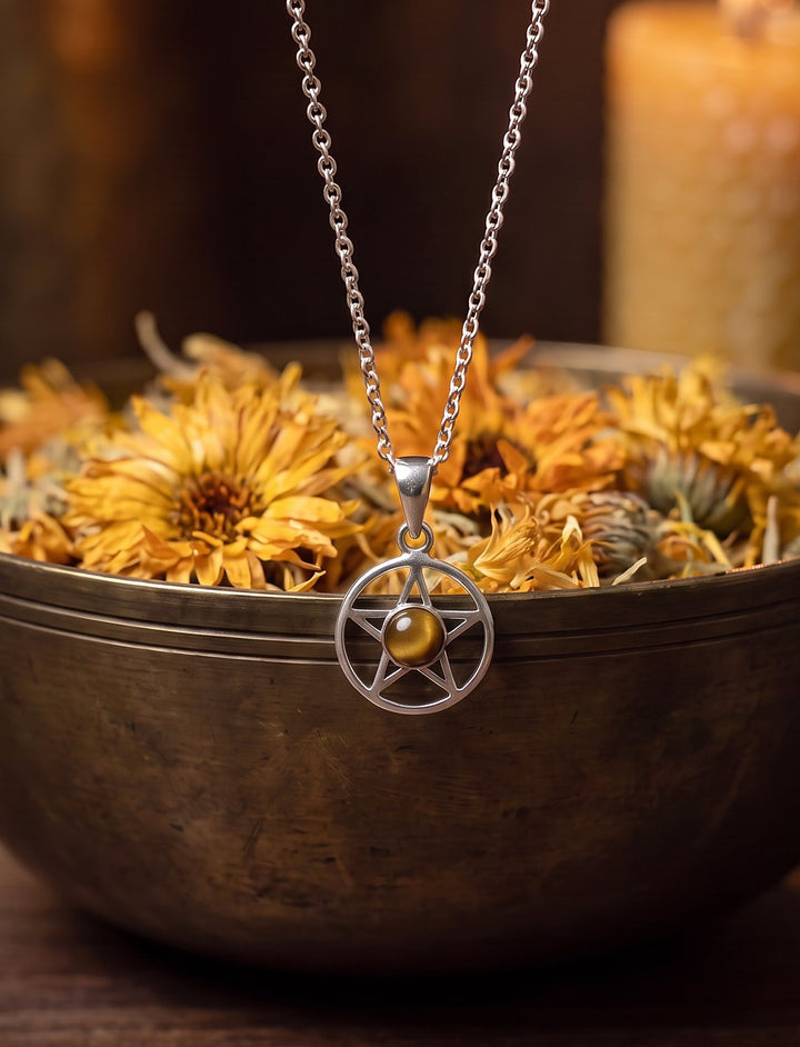 Fünfzackiger Stern im Kreis aus 925 Silber mit Tigerauge vor einer Messing-Altarschale mit getrockneten Ringelblumen