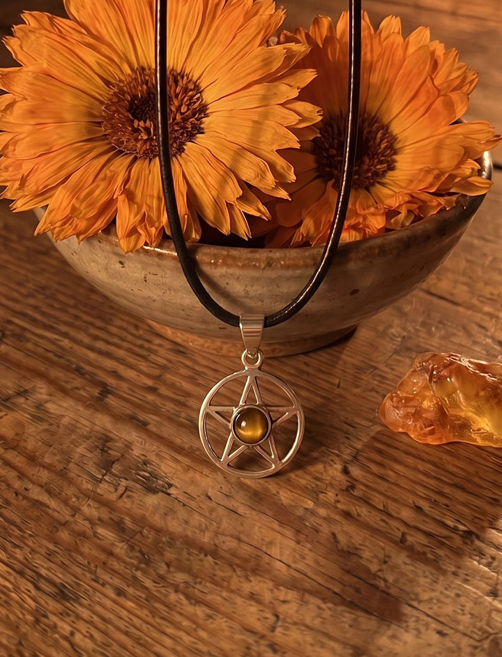 Pentagramm Anhänger mit Tigerauge an Lederkette vor einer Schale mit Ringelblumen und einem Stück Bernstein