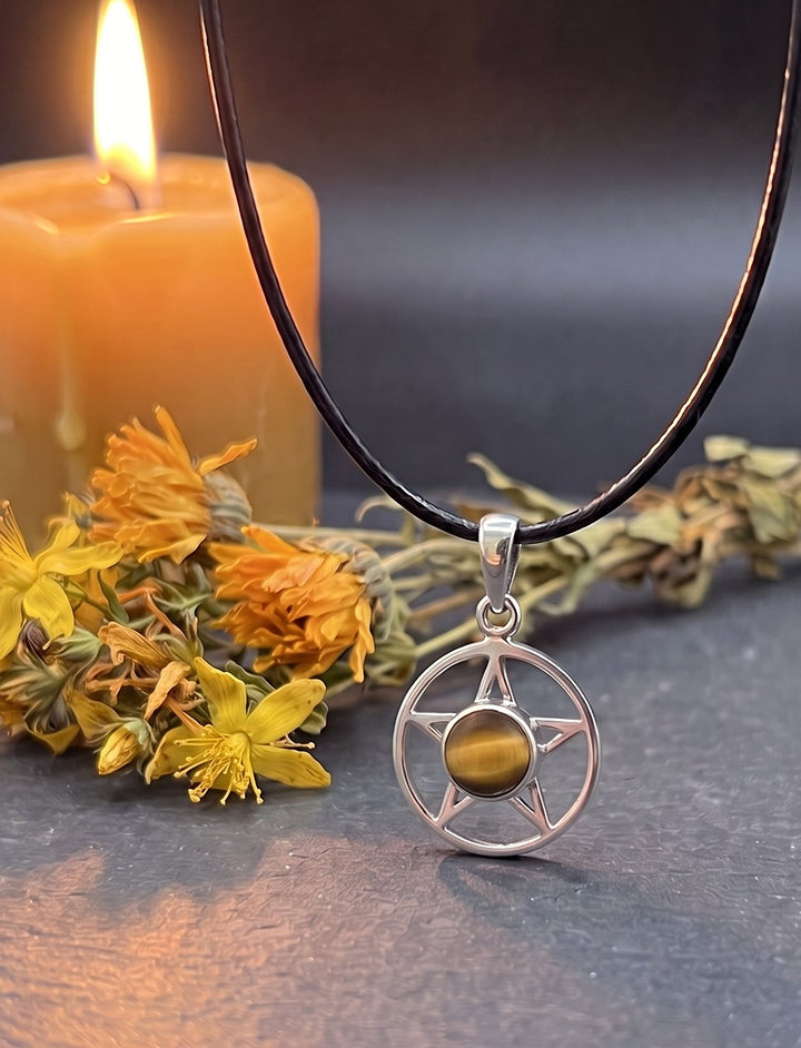 Sonnenstern: Pentagramm Kette aus Silber mit Tigerauge an schwarzer Lederkordel auf Schiefer neben Ringelblumen und Kerze