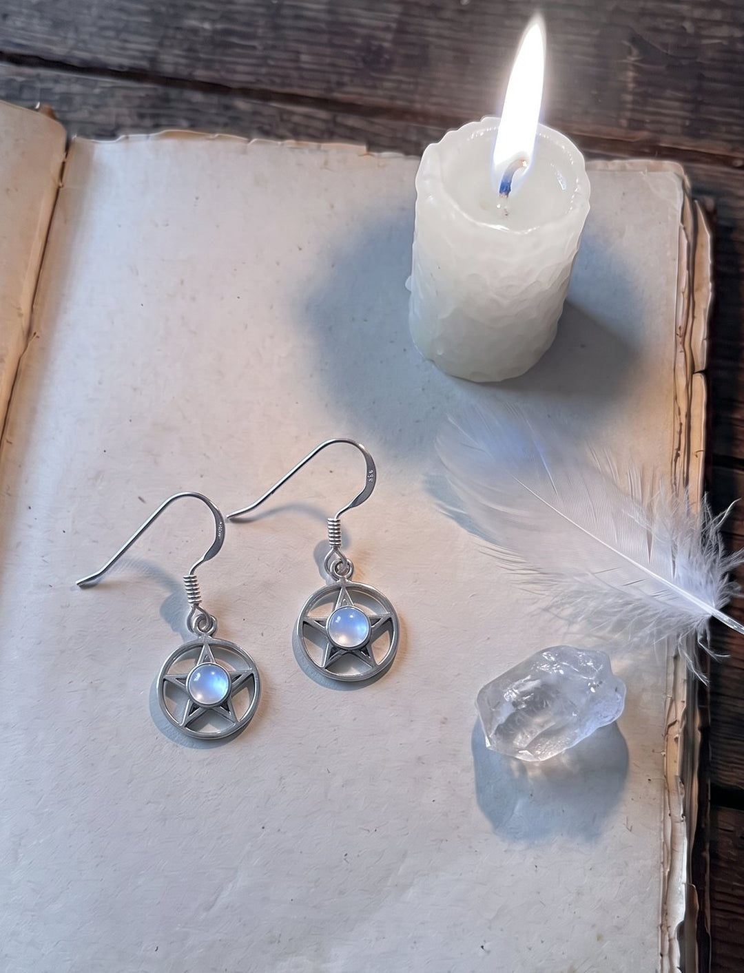 Ohrhänger aus 925 Silber mit fünfzackigem Stern und Mondstein auf einem alten Buch neben weißer Kerze und Bergkristall