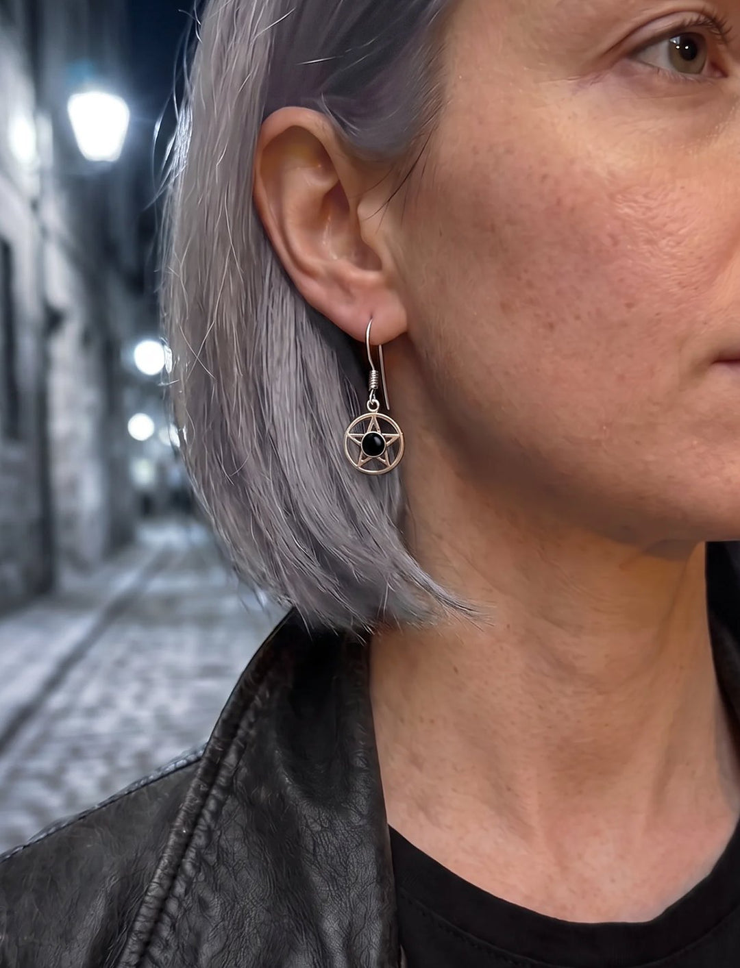 Frau mit grauem Bob und Lederjacke trägt Pentagramm Ohrringe mit Onyx in einer nächtlichen Gasse