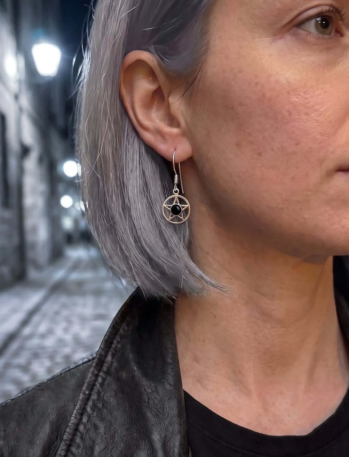 Frau mit grauem Bob und Lederjacke trägt Pentagramm Ohrringe mit Onyx in einer nächtlichen Gasse