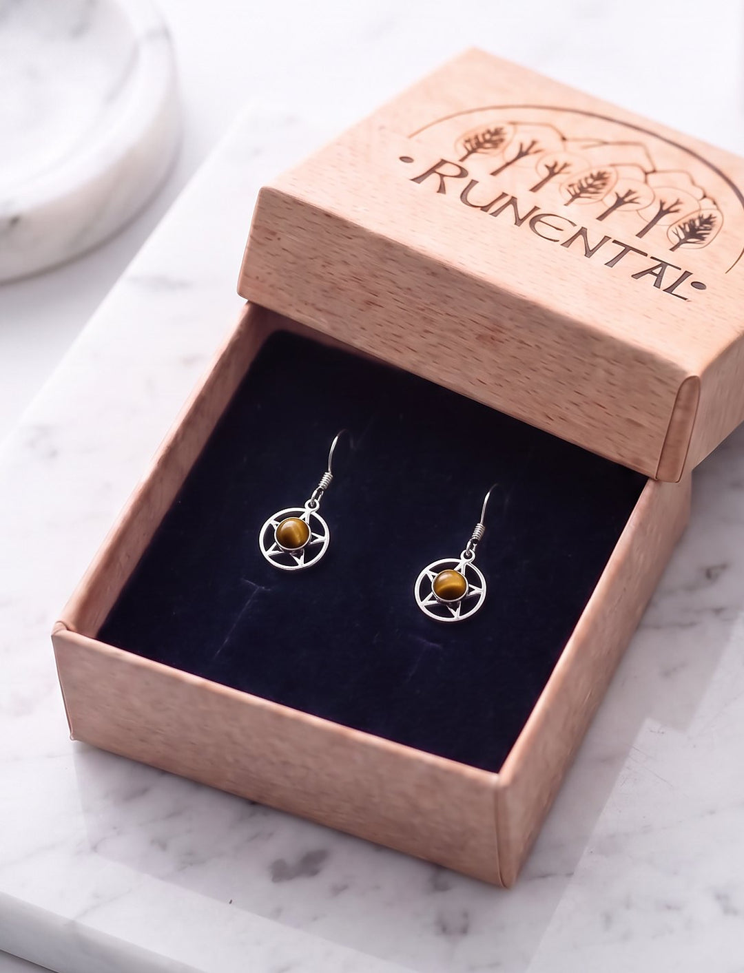 Pentagramm Ohrringe mit Tigerauge in der geöffneten Runental Geschenkbox auf weißem Marmor