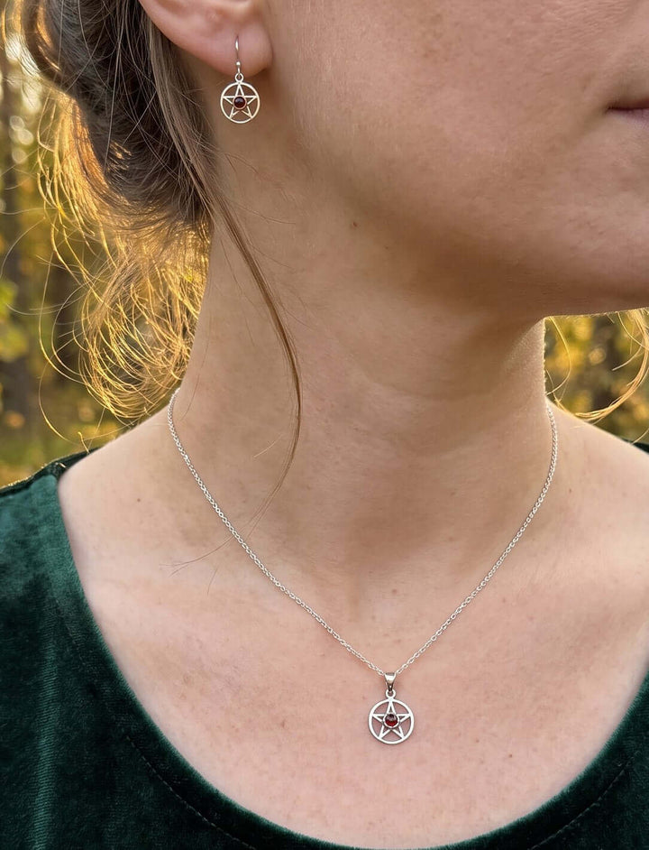 Frau mit hochgesteckten Haaren trägt Pentagramm Ohrringe und die passende Granat Kette aus Silber zu grünem Samt