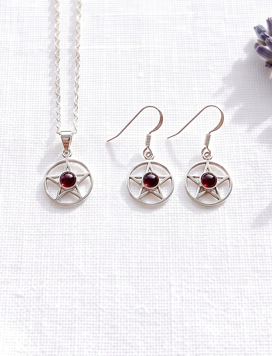 Schmuckset aus Pentagramm Kette und Ohrringen mit Granat in Silber auf weißem Leinen neben einem Lavendelzweig