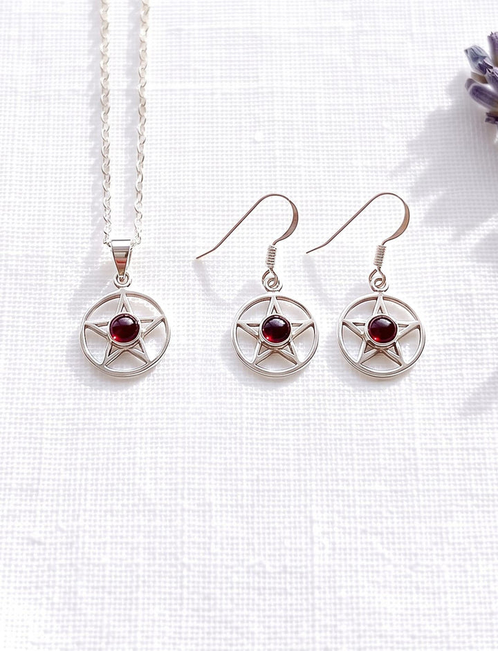 Schmuckset aus Pentagramm Kette und Ohrringen mit Granat in Silber auf weißem Leinen neben einem Lavendelzweig