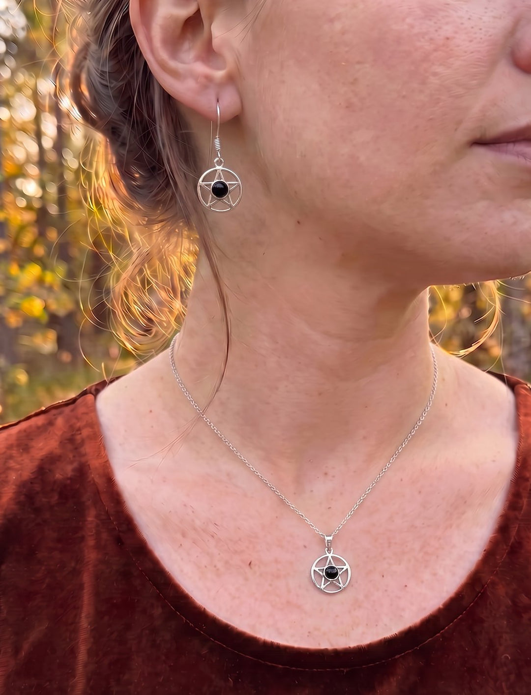 Frau mit hochgesteckten Haaren trägt Pentagramm Ohrringe und die passende Onyx Kette aus Silber zu rostrotem Samt