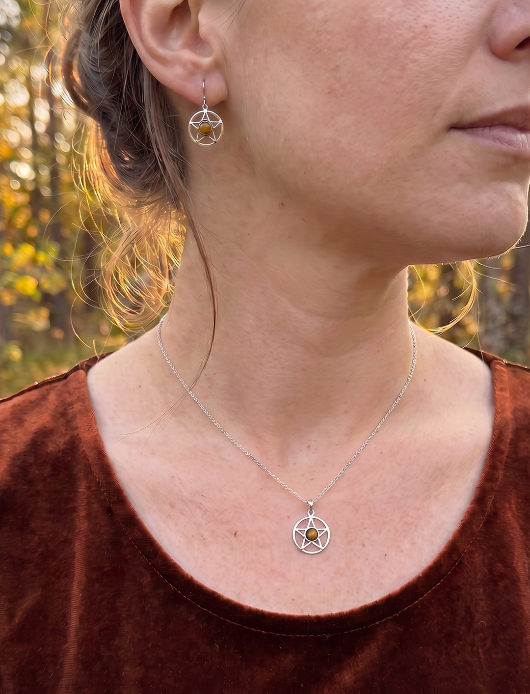 Frau im rostbraunen Samtoberteil trägt Pentagramm Ohrringe und die passende Tigerauge Kette im Herbstwald