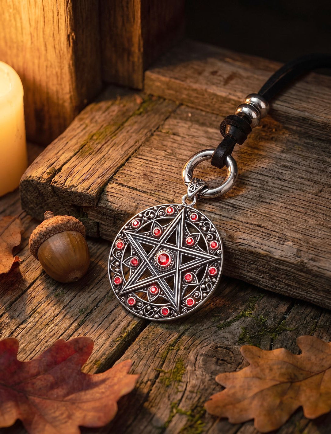 Pentagramm Anhänger mit roten Zirkonia am schwarzen Lederband mit Edelstahlring auf alter Eichenschwelle, daneben Eichel und Kerze