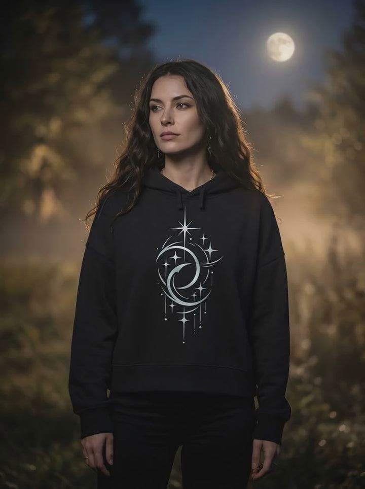 Video von Frau mit langen dunklen Haaren trägt schwarzen Bio Boxcut Hoodie mit Doppelmond Design bei warmem Mondlicht im Wald