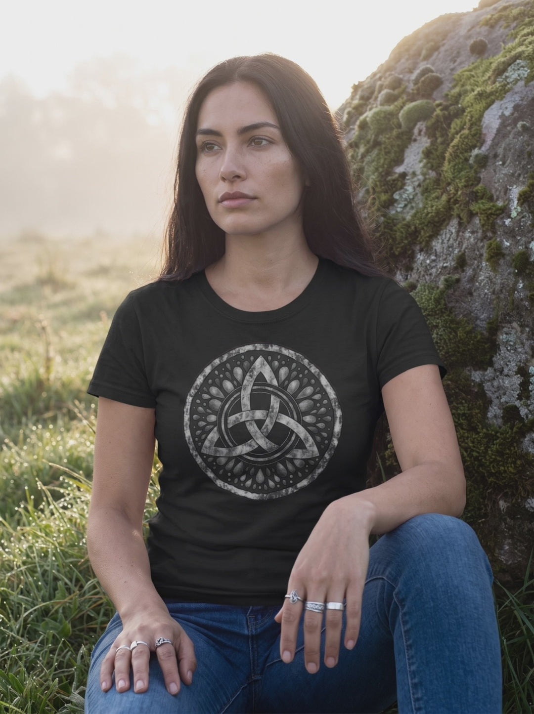 Video: Frau sitzt im schwarzen Damen Shirt auf einem Stein, die Kamera fährt langsam auf das Triquetra-Motiv zu