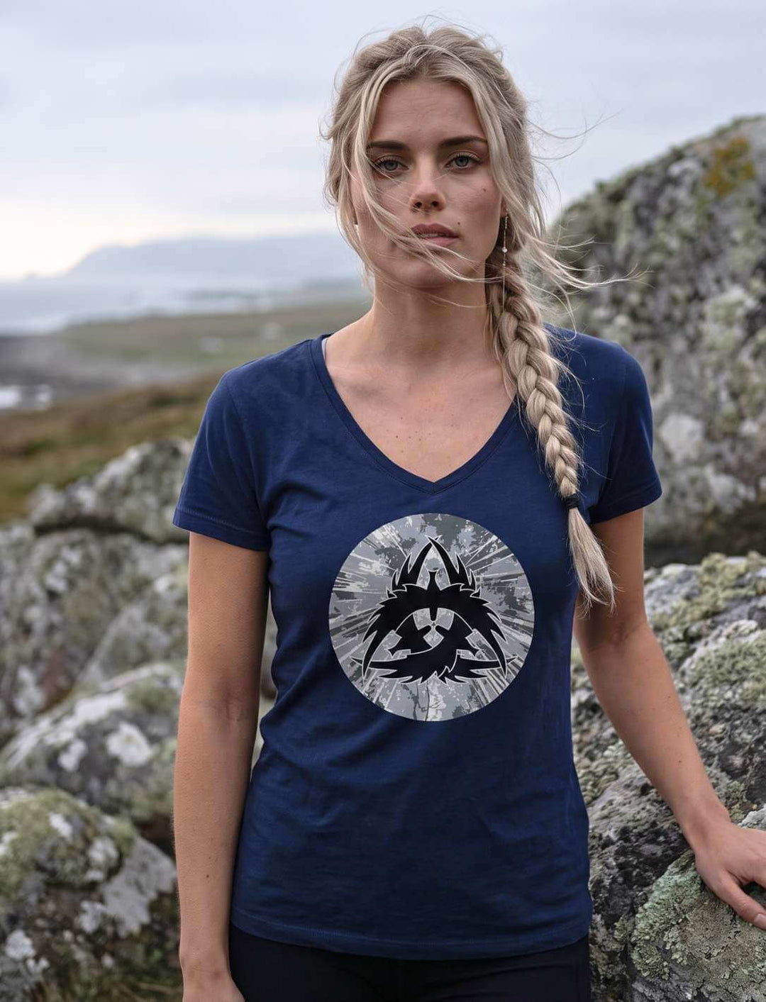 Navyfarbenes V-Neck Shirt mit Raben-Emblem, Frau vor grauem Meer und Wolkenhimmel