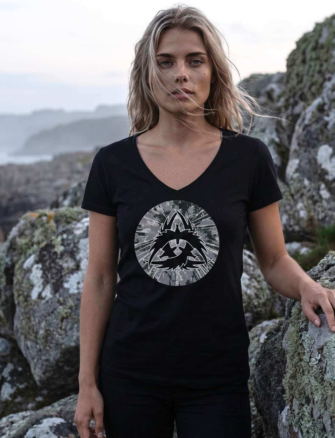 The Raven Clan Damen V-Neck Shirt in Schwarz mit nordischem Rabenzeichen, Frau vor Küstenfelsen