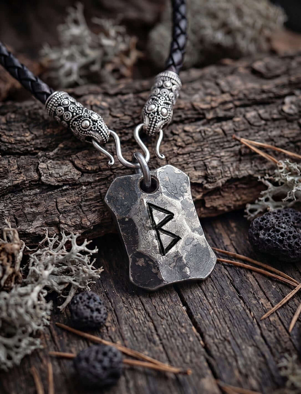 Berkano Rune Anhänger an geflochtener Lederkette mit versilberten Rabenköpfen auf Rinde mit Flechten und Lavasteinen