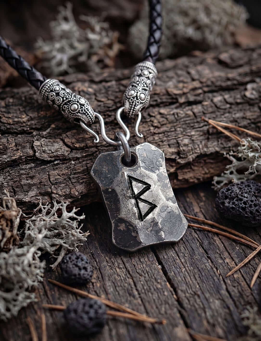 Berkano Rune Anhänger an geflochtener Lederkette mit versilberten Rabenköpfen auf Rinde mit Flechten und Lavasteinen