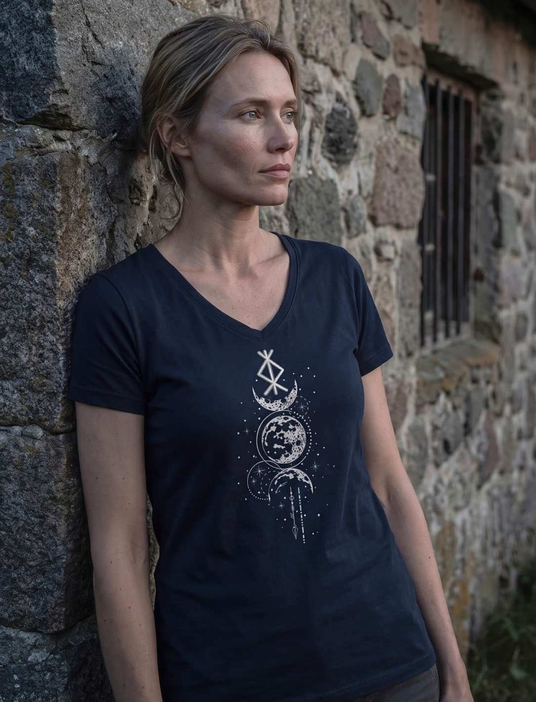 Frau im blauen V-Neck Shirt an einer Feldsteinmauer, Binderune im Seitenlicht