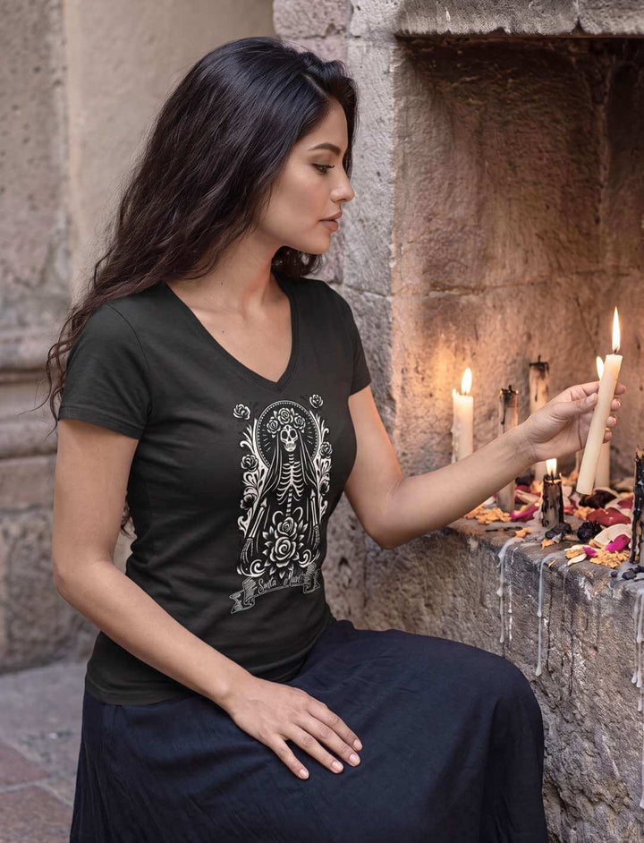 Damen V-Neck Shirt in Schwarz vor einer Wandnische voller brennender Kerzen