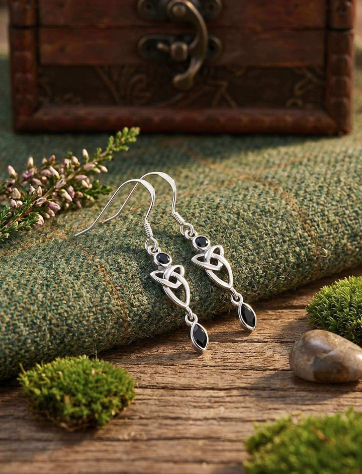 Schwarze Triquetra Silber Ohrhänger mit Onyx auf grünem Stoff und Holz